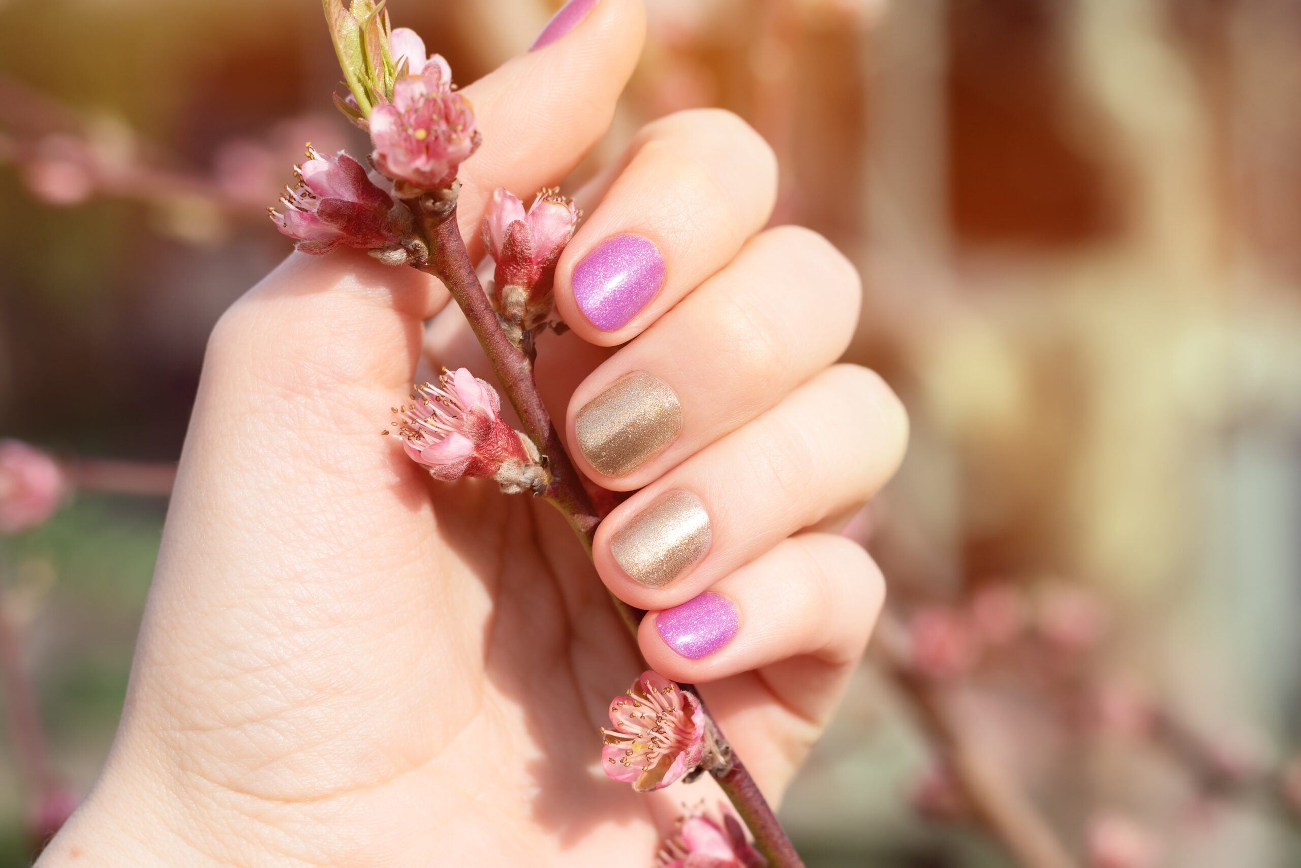female-hand-with-gold-purple-nail-design-holding-blossom-branch-min